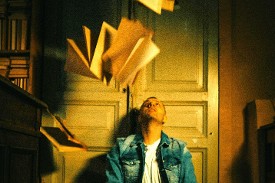A young man seated on the floor looks up at books thrown in the air (Photo Nadin Sh for Pexels)